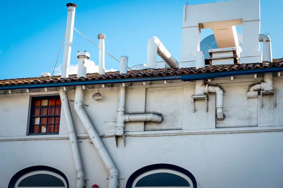 Conduits et tuyaux blancs le long d'une façade et au-dessus d'un toit de tuiles