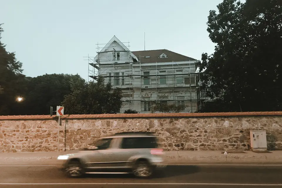 Maison ancienne entourée d'un échafaudage, derrière un mur de pierre longé par une voiture
