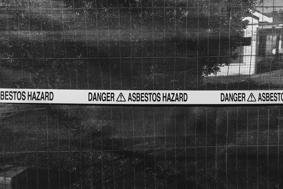 Ruban de danger signalant la présence d'amiante, tendu sur une clôture de chantier, en noir et blanc