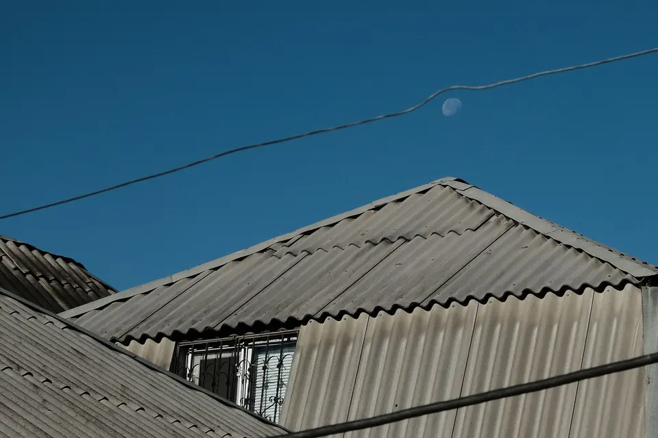 Toit couvert de plaques ondulées grises, sous un ciel bleu traversé par un câble
